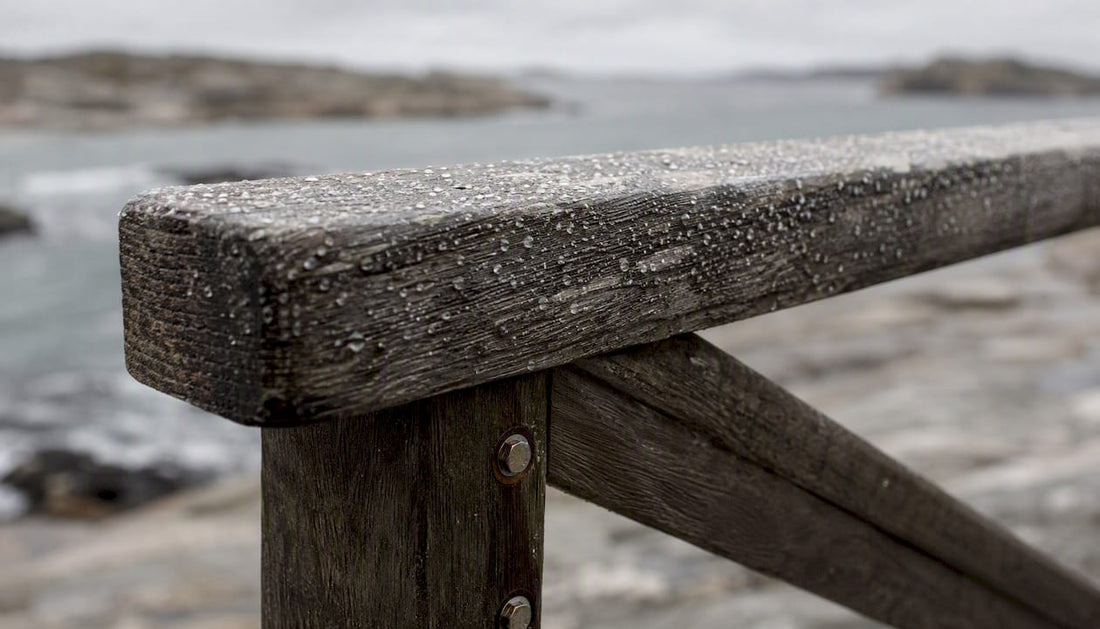 Solenblekt och vindpinad träarmstöd på en utestol intill havet