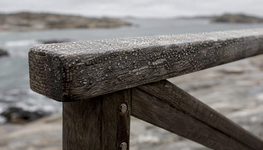 Solenblekt och vindpinad träarmstöd på en utestol intill havet